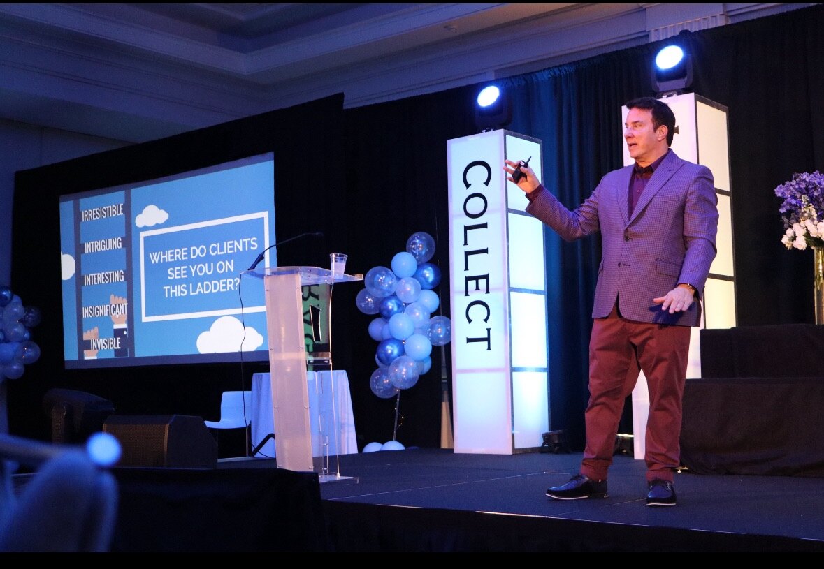 1-john-keynote-stage John Livesay speaking onstage beside a presentation about standing out to clients.